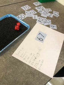 Bilden visar en "mattebricka" med tillhörande tärningar, positionskort och ett papper med huvudräkningsstrategier nedskrivna av elever.
